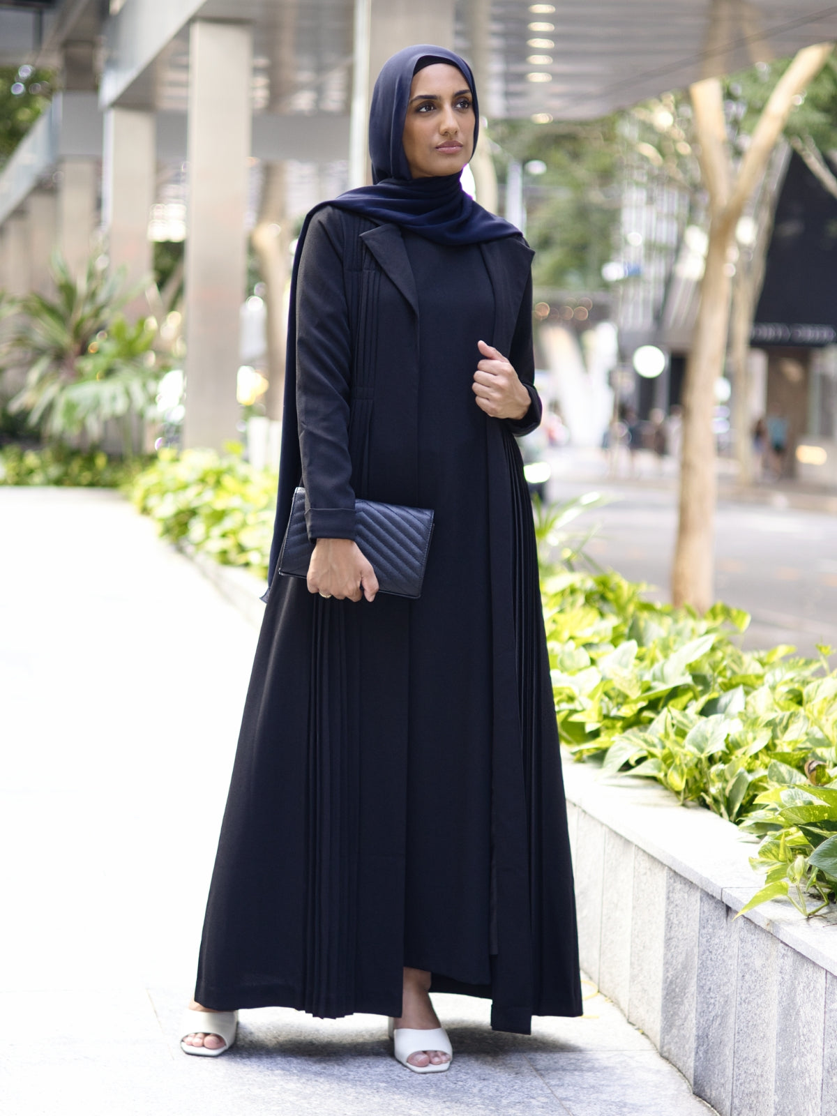 Muslim woman wearing the Amani Pleated Blazer Set in black, standing confidently in a city street, showcasing elegant and modest formal fashion.
